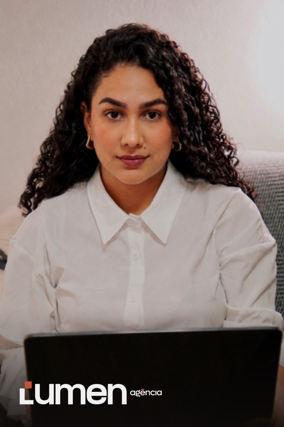 Integrante da equipe da Lumen Agência com o notebook, olhando para a frente, com a logo da agência